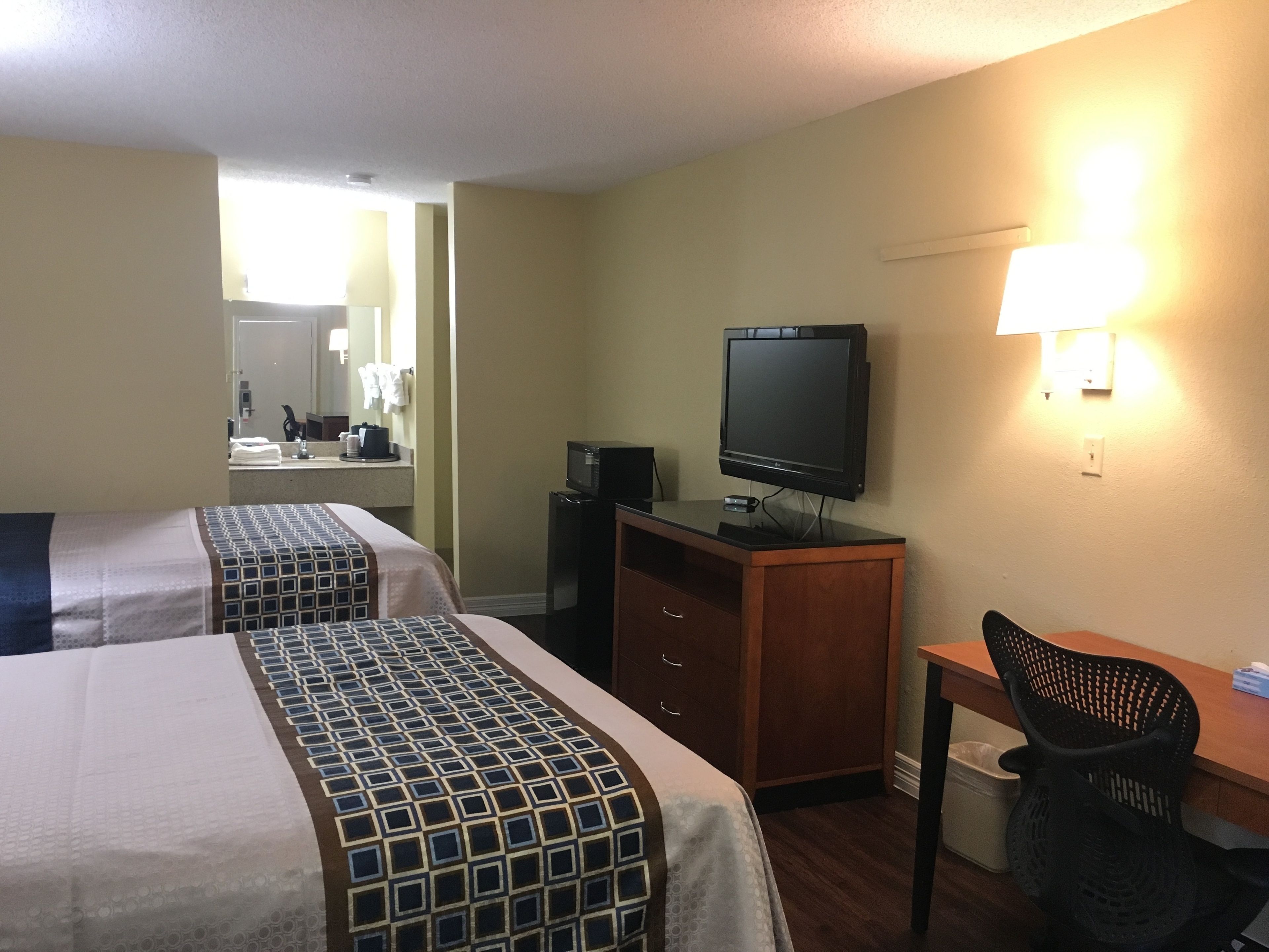A hotel room with two beds, a desk with a television, a chair, and a trash bin.