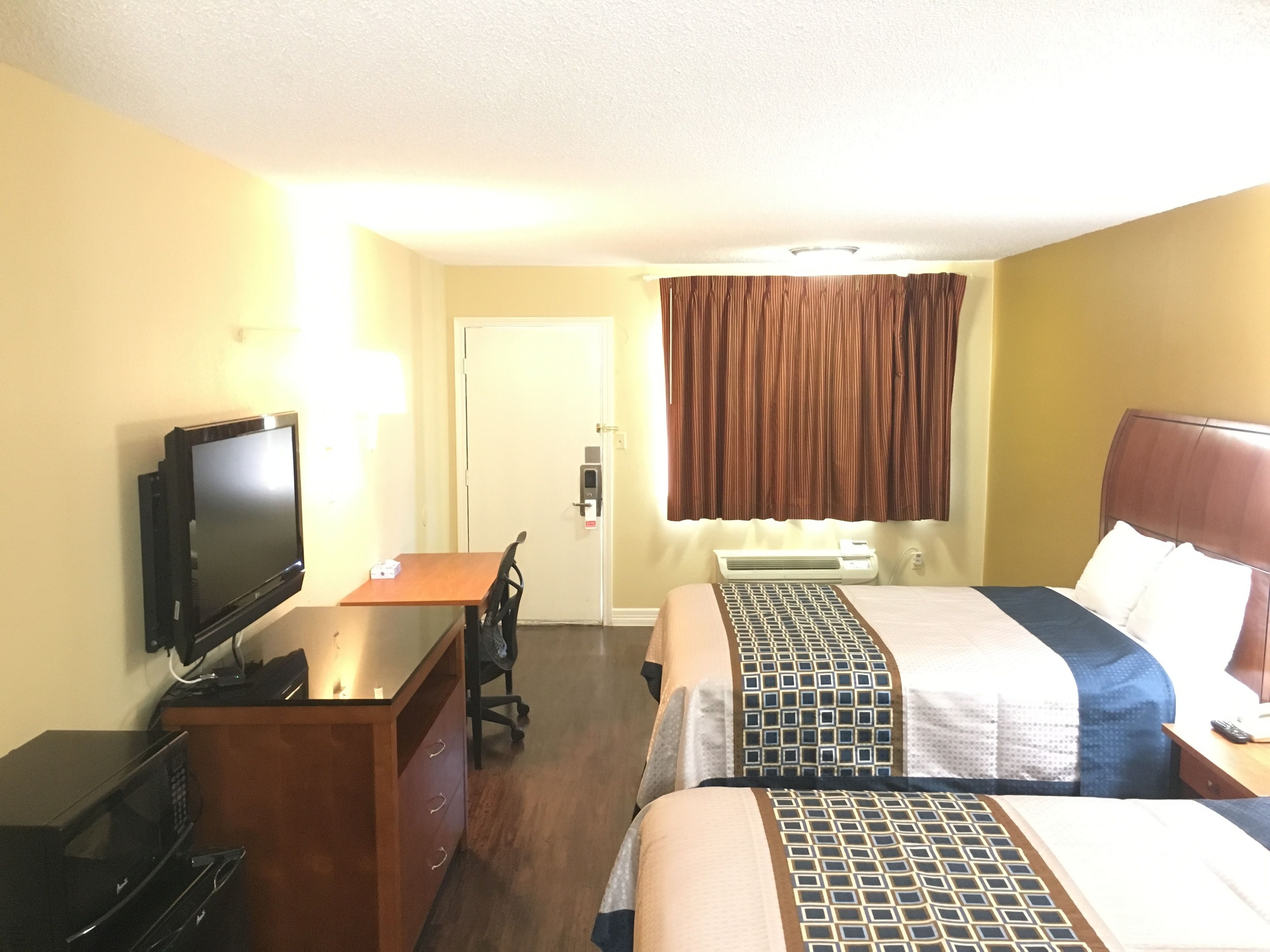 Ein Hotelzimmer mit einem Bett, einem Schreibtisch mit Fernseher, einer Mikrowelle und einer Klimaanlage.