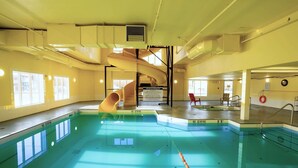 An indoor swimming pool with a spiral slide, clear pool edges, and no diving signs. - Ramada by Wyndham Cranbrook (Cranbrook)