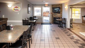 A restaurant with multiple tables and chairs, a television mounted on the wall, and a fireplace. - Ramada by Wyndham Cranbrook (Cranbrook)