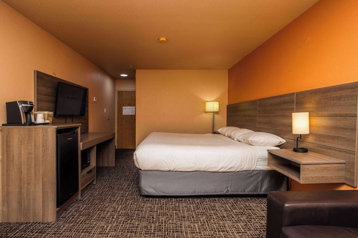 A hotel room with a bed, a desk with a lamp, a TV, and a coffee machine.