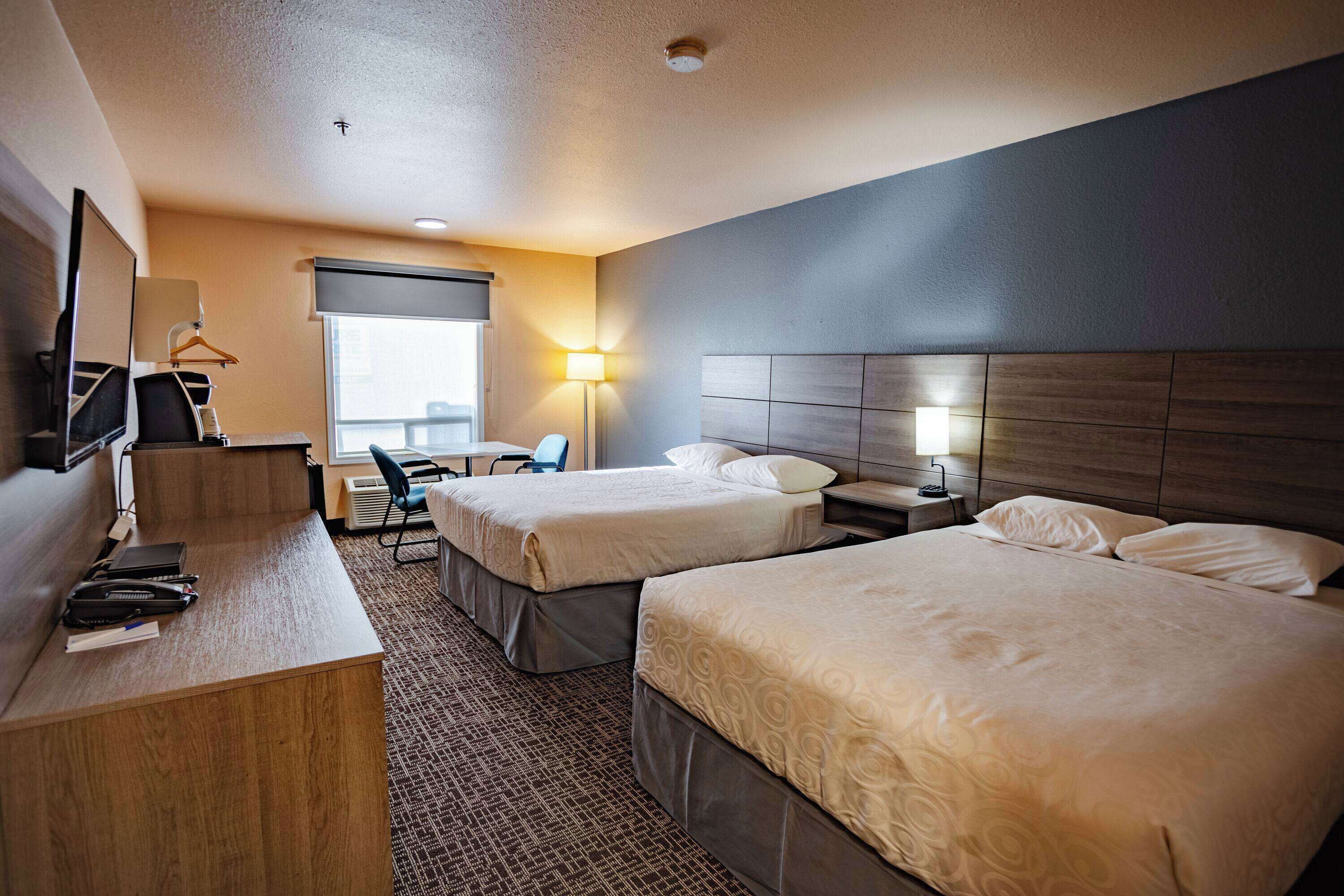 A hotel room with two beds, a desk, a chair, a TV, and a window.