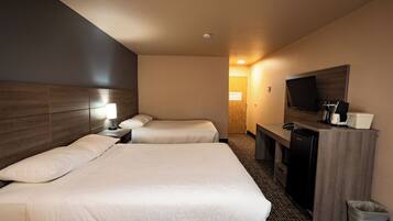 A hotel room with two beds, a desk with a TV, a refrigerator, and a trash bin.