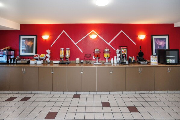A hotel reception area with a red wall, a counter with various amenities, and a tiled floor. - Ramada by Wyndham Cranbrook (Cranbrook)