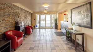 A hotel lobby with a brick wall, red leather chairs, a reception desk, and a framed picture on the wall. - Ramada by Wyndham Cranbrook (Cranbrook)