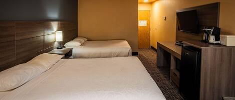 A hotel room with two beds, a desk with a TV, and a coffee maker.