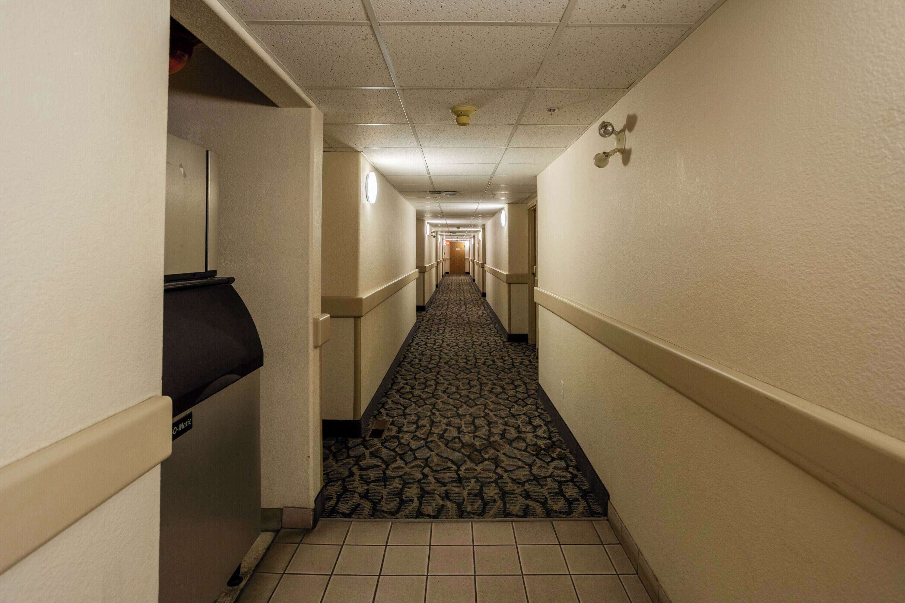 A long, narrow hallway with patterned carpet, tiled floors, and cream-colored walls.