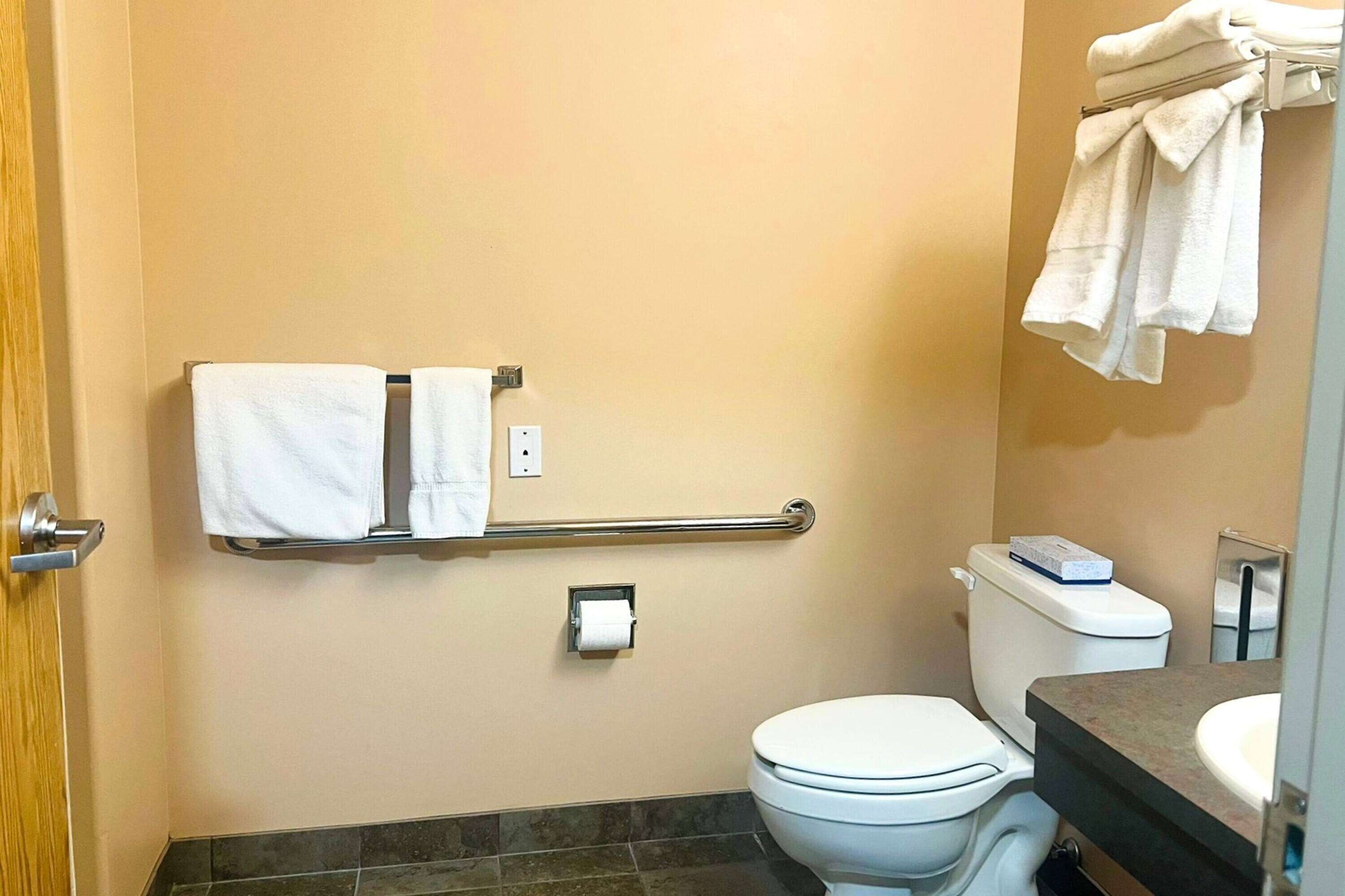 A bathroom with a toilet, a towel rack with towels, a paper towel dispenser, and a sink.