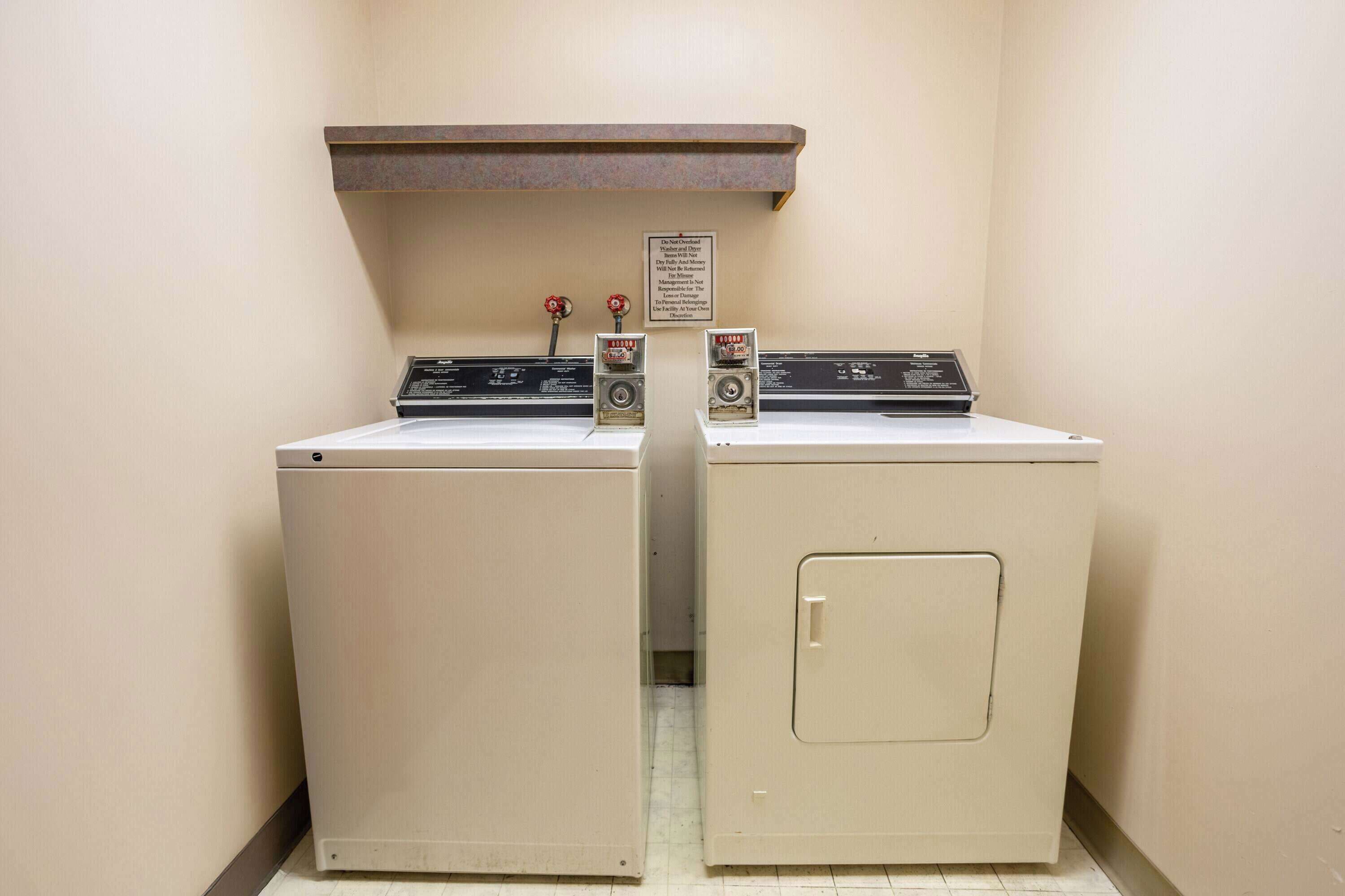 A laundry room with two washers and a dryer, a sign above the dryers, and a vent above the washers.