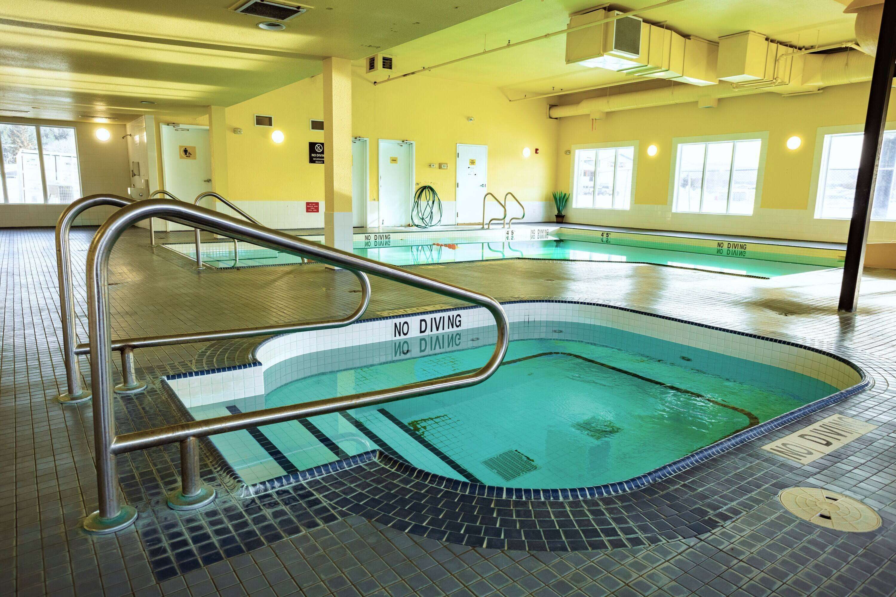 An indoor swimming pool with a 'No Diving' sign, tiled walls, and a metal handrail.