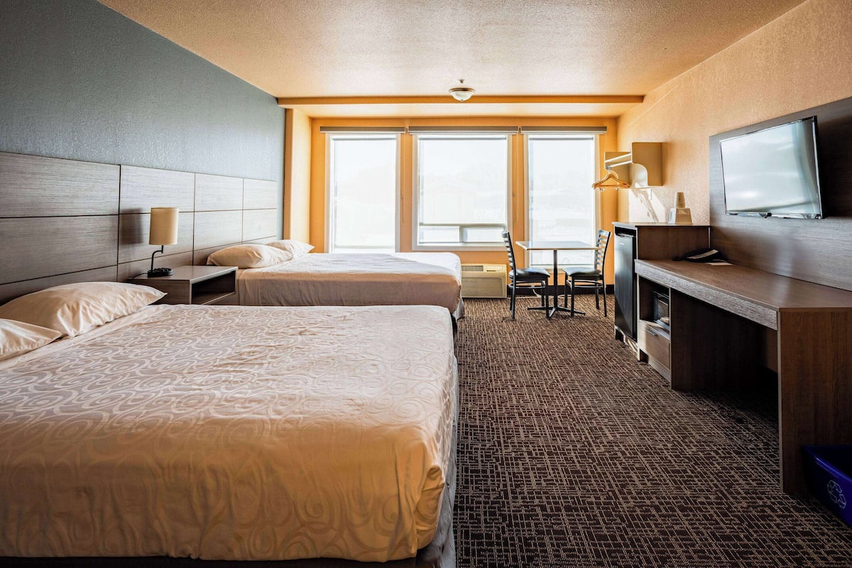 A hotel room with two beds, a desk, a television, and large windows.