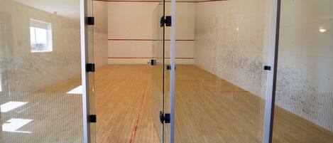 A squash court with glass doors, wooden floor, and a window.