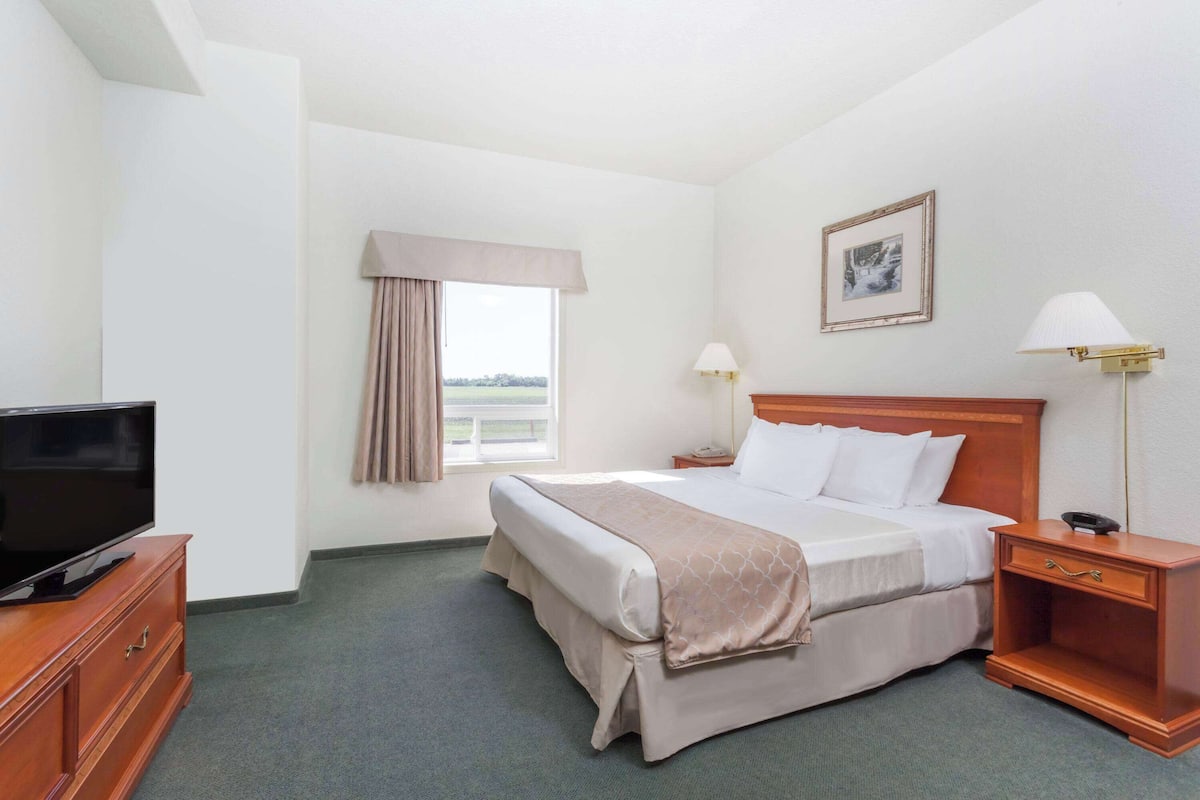 A hotel room with a bed, bedside lamps, a TV on a wooden cabinet, and a window with curtains.