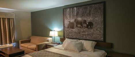 Een hotelkamer met een groot bed, een stoel, een nachtkastje en een wandlamp.