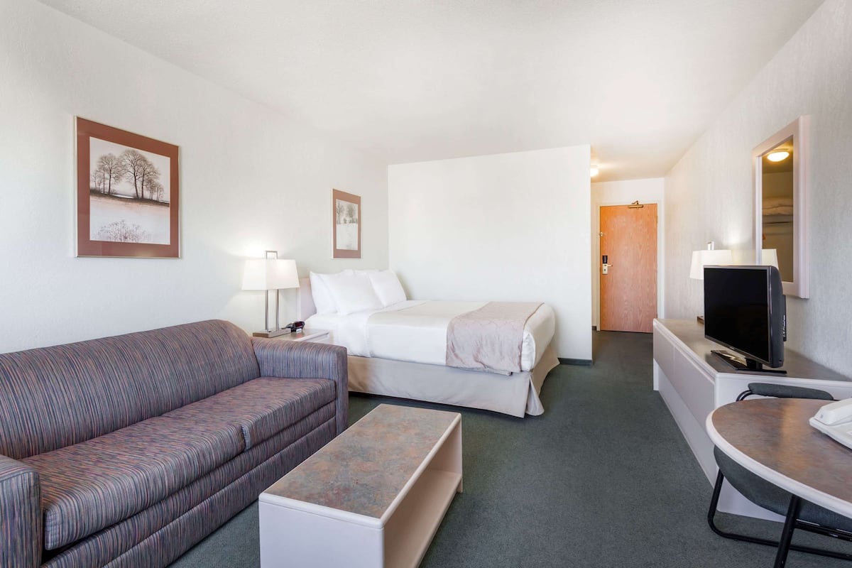 A hotel room with a sofa, a bed, a small table, a TV, and framed pictures on the wall.
