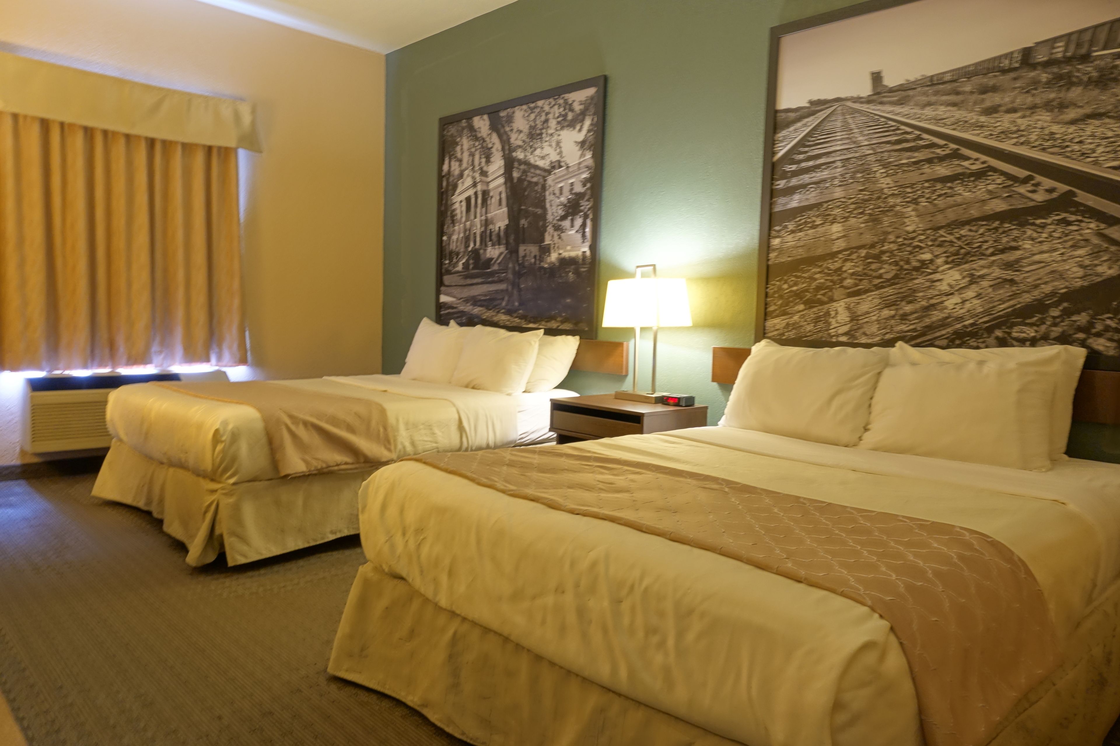 A hotel room with two beds, a nightstand, a lamp, and a large framed picture on the wall.