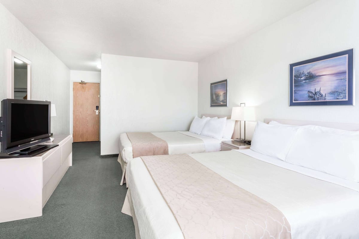 A hotel room with two beds, a TV, a painting, and a door leading to a bathroom.