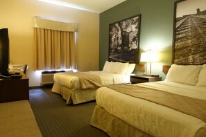 Una habitación de hotel con dos camas, un escritorio con computadora, un televisor y una ventana con cortinas.