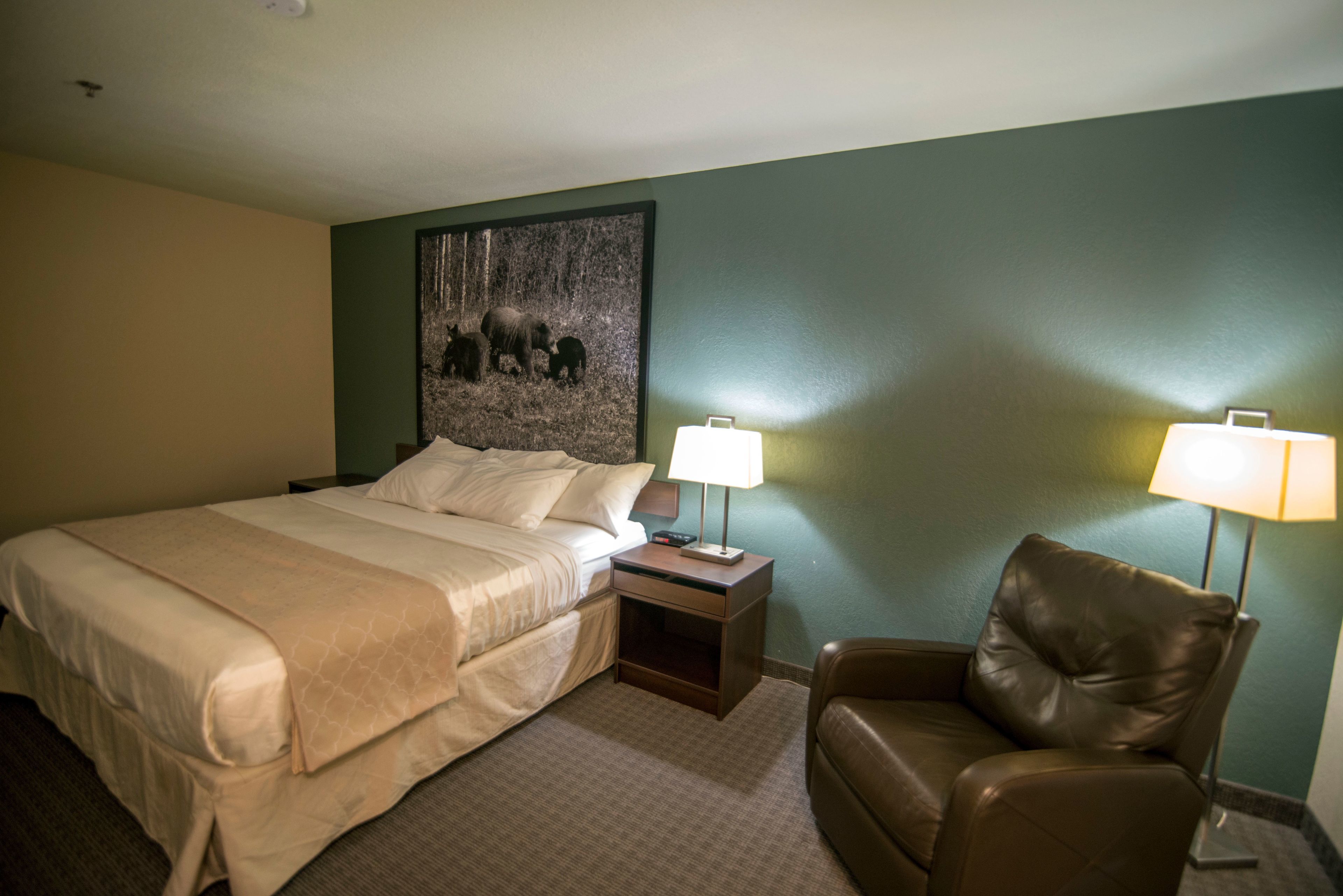 A hotel room with a large bed, two bedside lamps, a brown leather chair, and a wall-mounted painting.