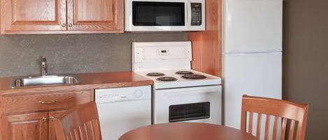 A compact kitchen with wooden cabinets, a microwave, a stove, a dishwasher, and a refrigerator.