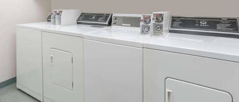 A laundry facility with four white washing machines and a control panel.