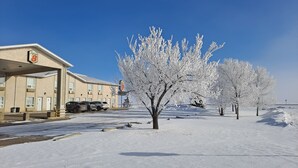 A Super 8 motel with a parking lot and snow-covered trees. - Super 8 by Wyndham Three Hills AB (Three Hills)
