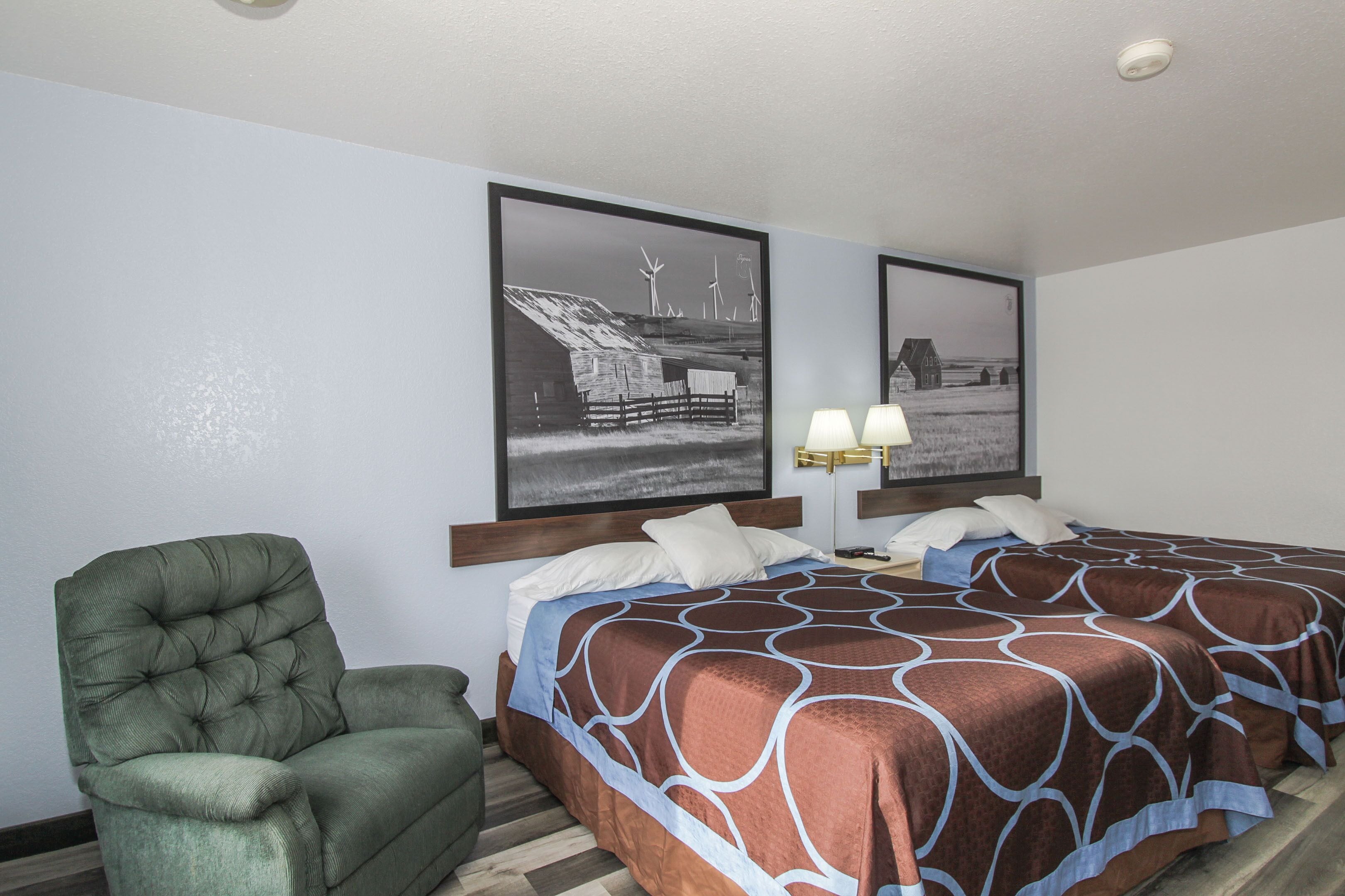 Habitación de hotel con una cama, dos lámparas de pared, un sillón verde y dos cuadros en la pared.
