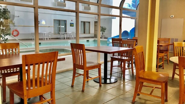 A poolside area with wooden tables and chairs, a clear view of the pool, and a large window with a view of the pool and outside. - Super 8 by Wyndham Three Hills AB (Three Hills)