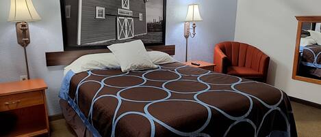 A hotel room with a large bed, two bedside tables, a chair, a mirror, and a wall-mounted lamp.