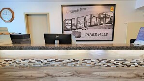 A reception desk with a framed welcome sign, a clock, and a Dell computer. - Super 8 by Wyndham Three Hills AB (Three Hills)