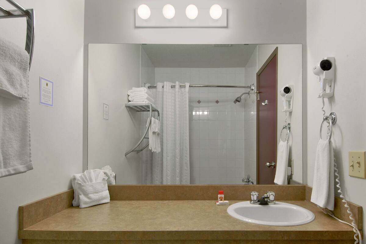 Ein Badezimmer mit Waschbecken, Spiegel, Handtuchhalter, Duschvorhang und einem an der Wand befestigten Föhn.