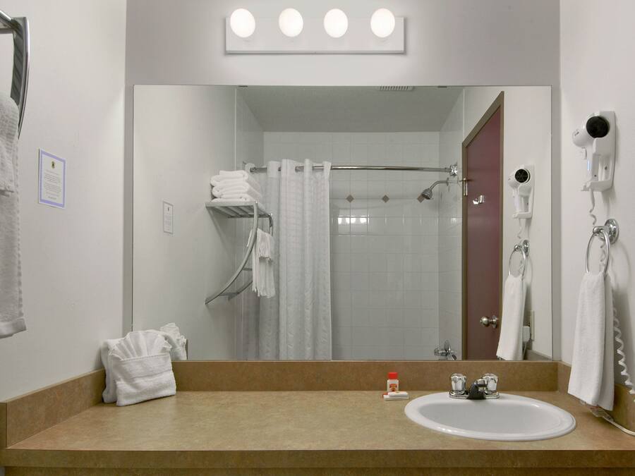 A bathroom with a sink, mirror, towel rack, shower curtain, and a hairdryer mounted on the wall.