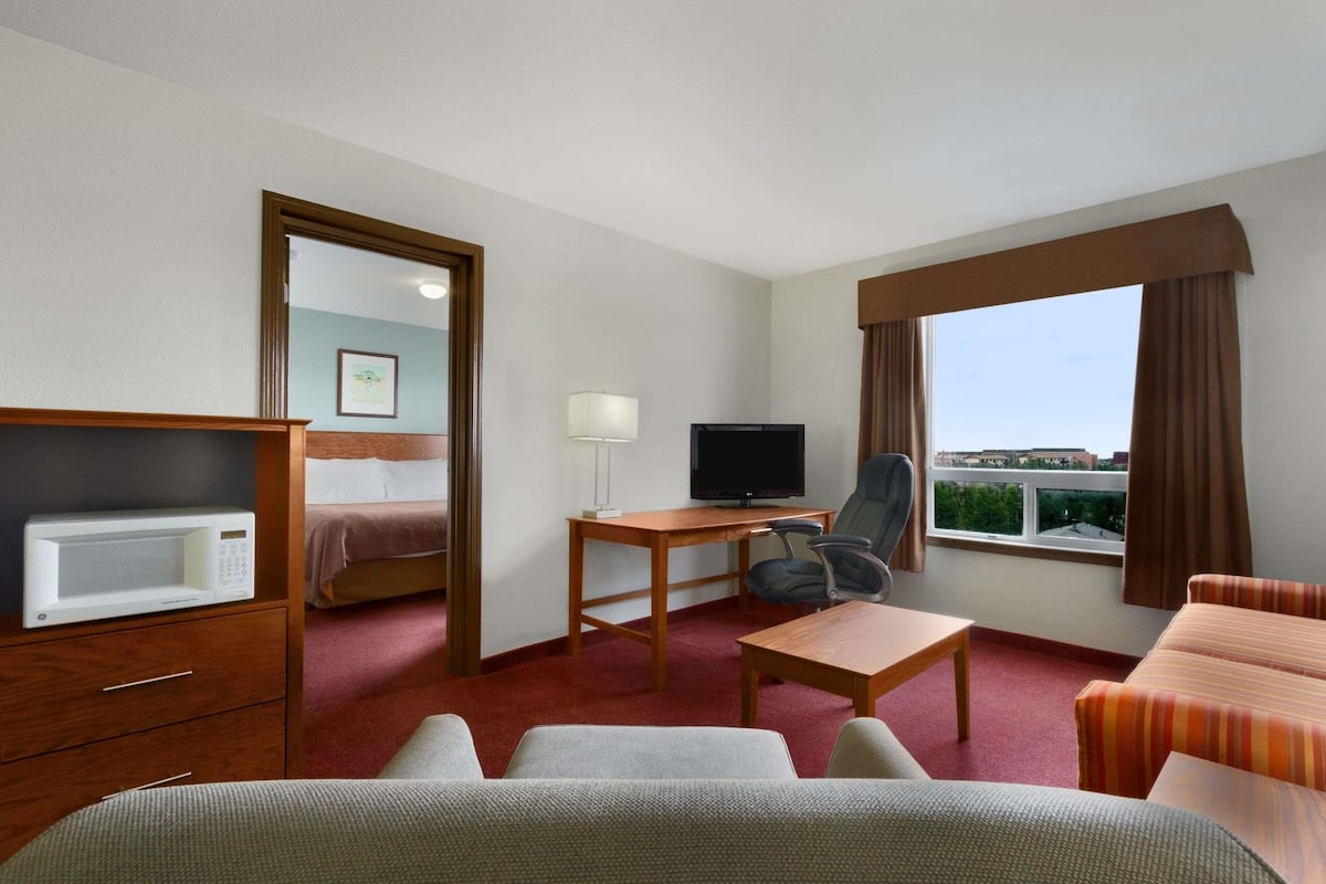 Ein Hotelzimmer mit einem Bett, einem Schreibtisch mit Fernseher, einer Mikrowelle, einem Sessel und Blick auf die Stadt durch das Fenster.