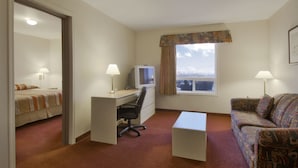 A hotel room with a bed, a desk with a computer, a chair, a sofa, and a window with a view.