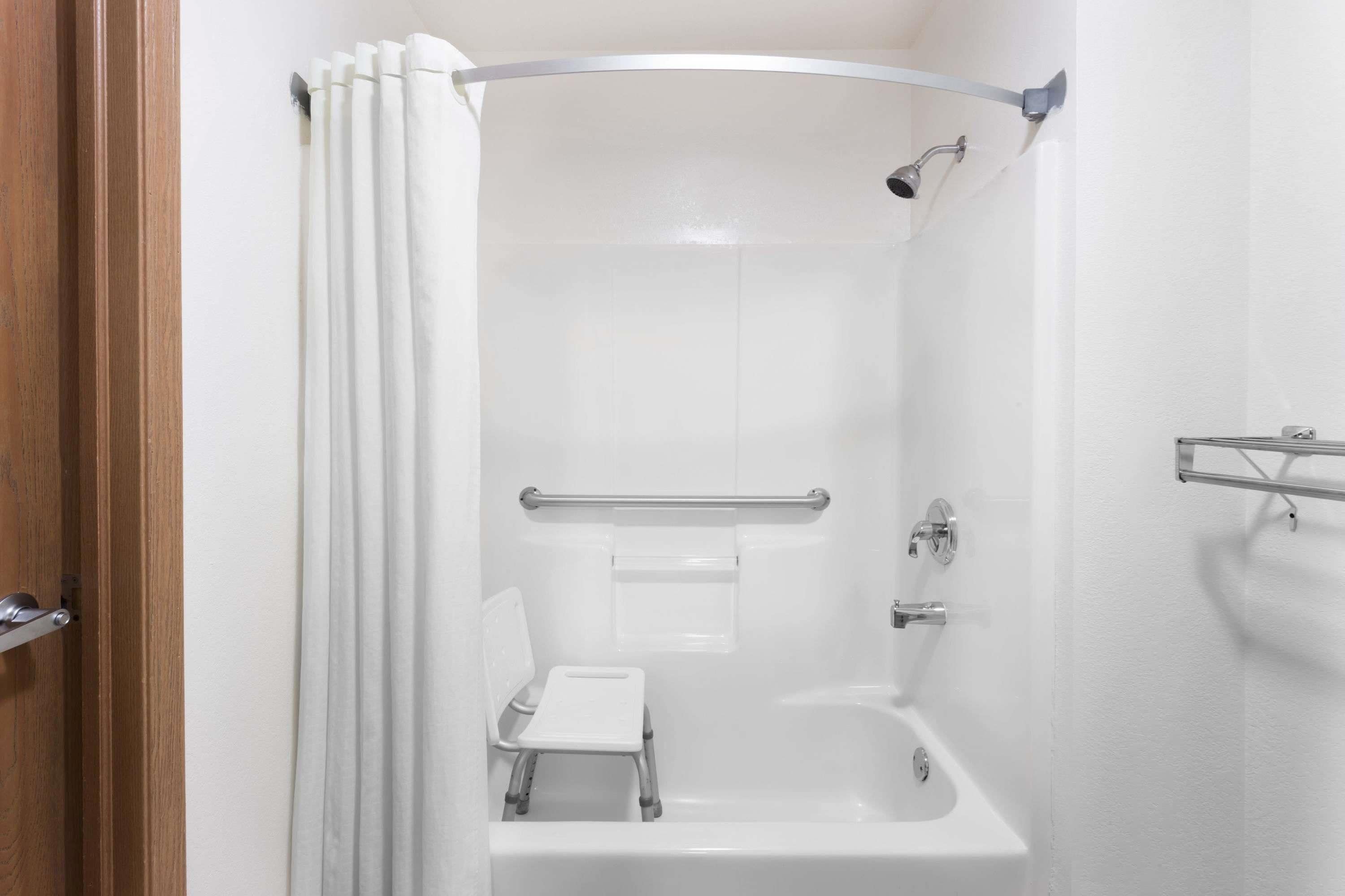 Ein modernes Badezimmer mit Dusche, einer kleinen Stehgehhilfe und einer Haltestange.