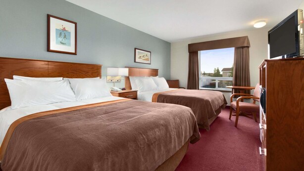 A hotel room with two beds, a television, a desk, and a window with curtains.