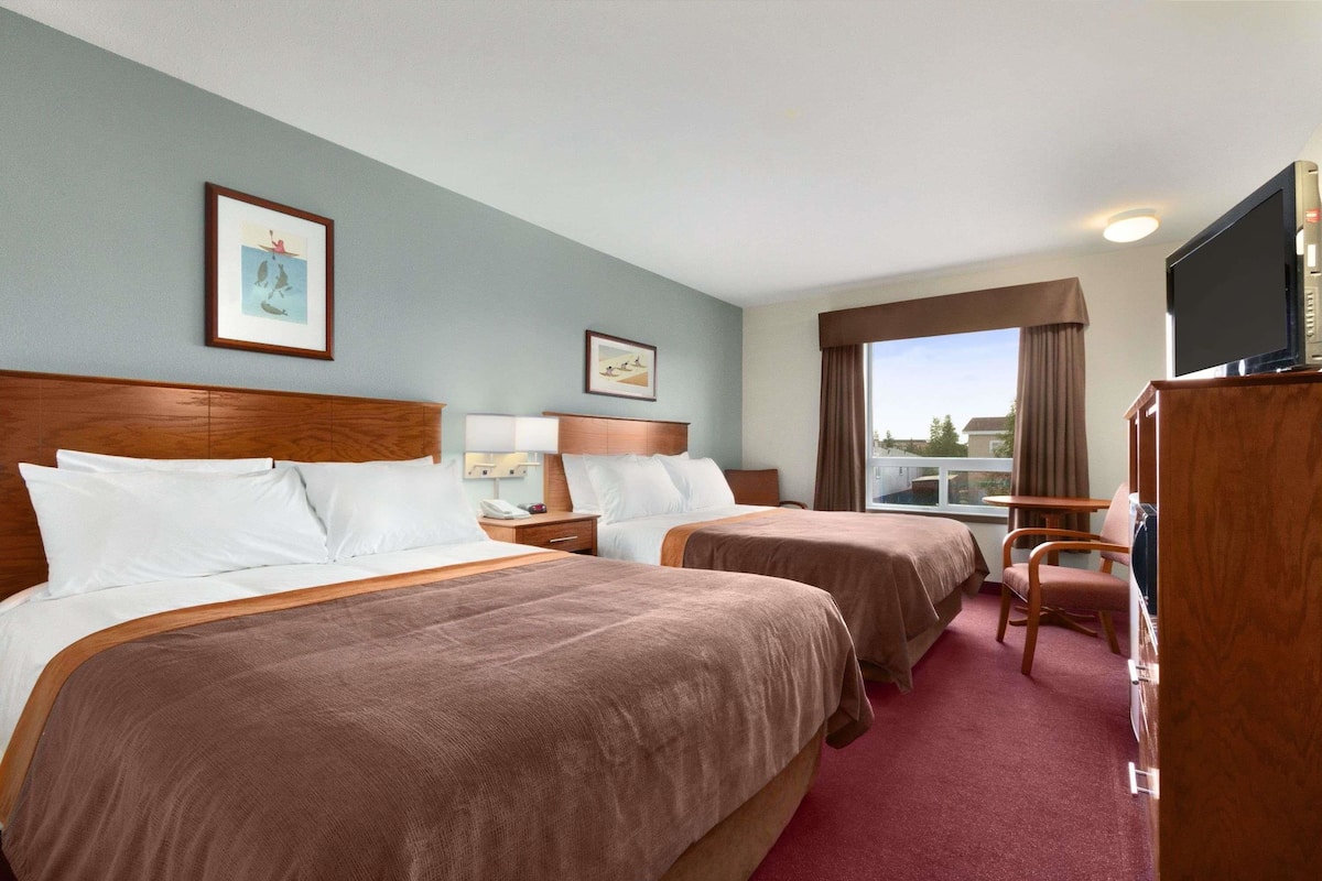 Ein Hotelzimmer mit zwei Betten, einem Fernseher, einem Schreibtisch und einem Vorhangfenster.