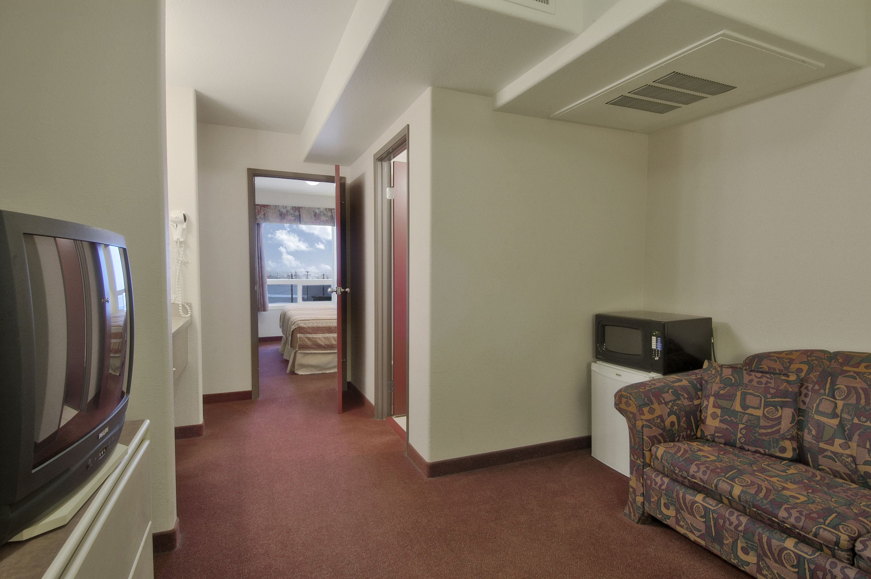 A hotel room with a television, a sofa, and a small desk with a microwave.