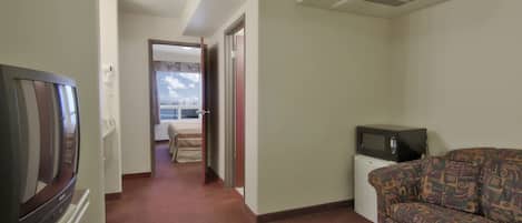 A hotel room with a television, a sofa, and a small desk with a microwave.