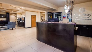 A hotel reception area with a reception desk, a seating area with a patterned armchair, and a wall-mounted sign for SureStay Plus Hotel by Best Western. - SureStay Plus by Best Western San Antonio Airport (San Antonio)
