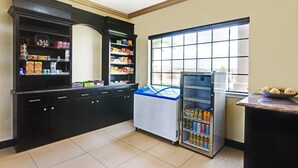 A kitchen with a refrigerator, shelves with snacks, and a window. - SureStay Plus by Best Western San Antonio Airport (San Antonio)