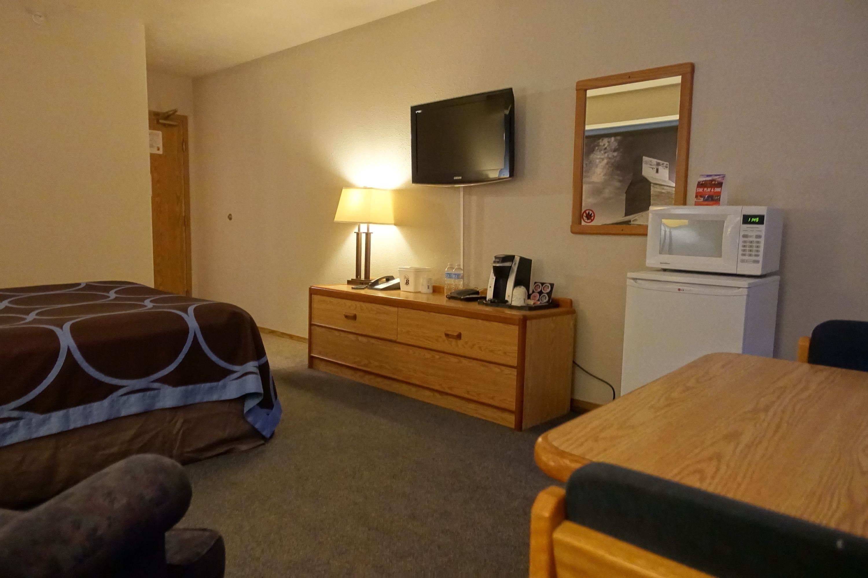 Une chambre d’hôtel comprenant un lit, une commode en bois, un bureau, un four à micro-ondes, une télévision et une lampe.