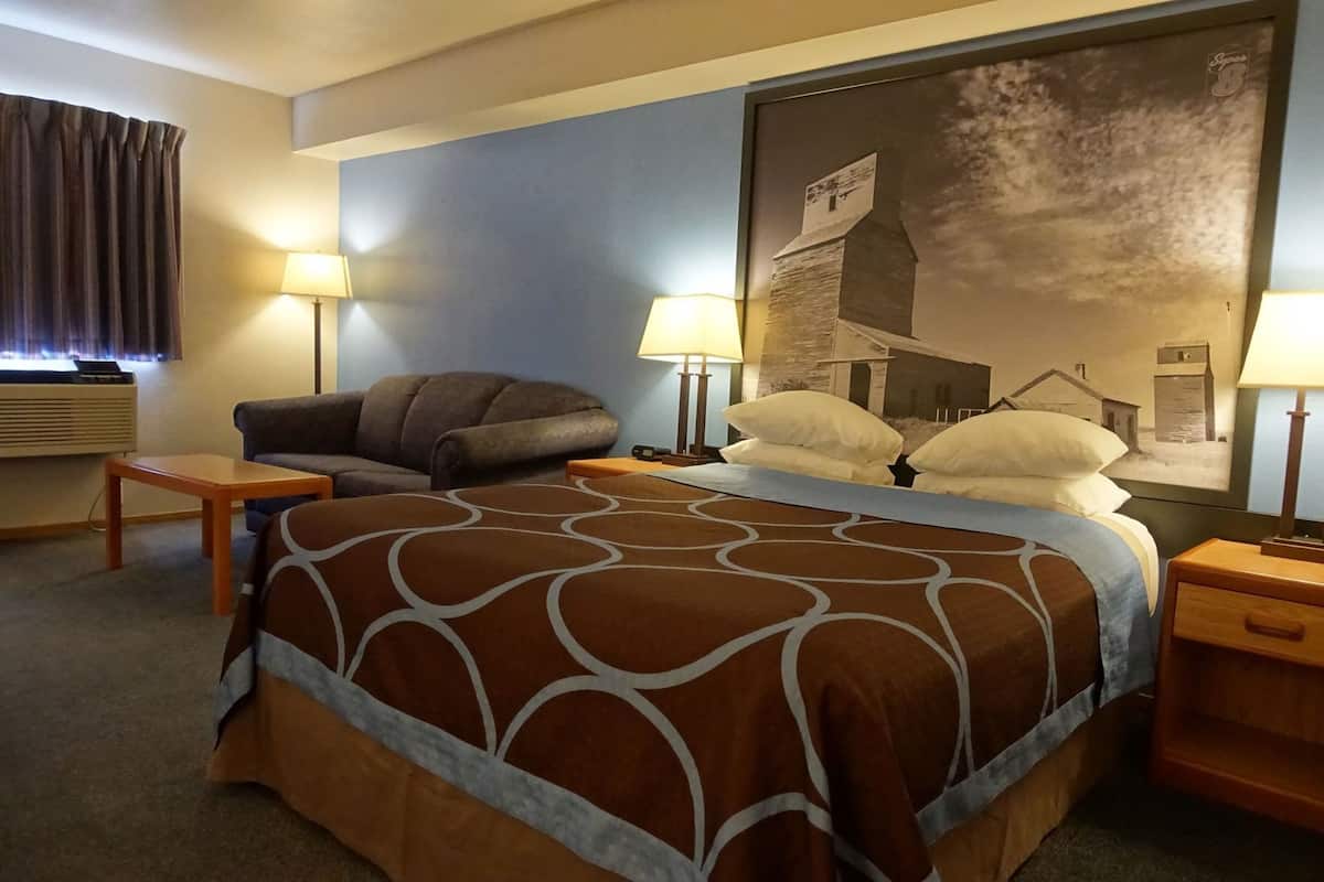 A hotel room with a bed, two bedside tables, a chair, a lamp, and a wall-mounted painting.