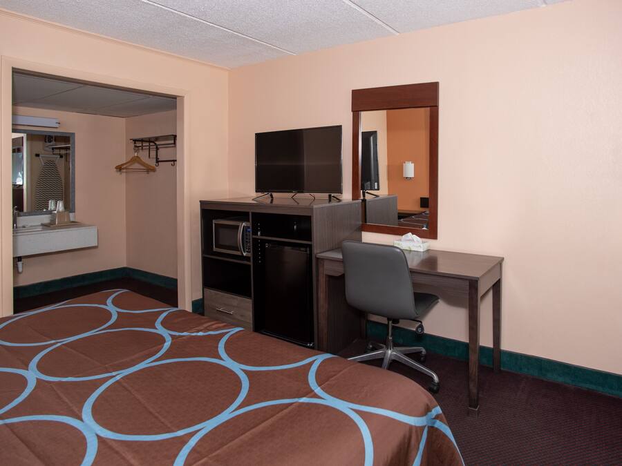 A hotel room with a bed, a desk, a television, a mirror, and a kitchenette.