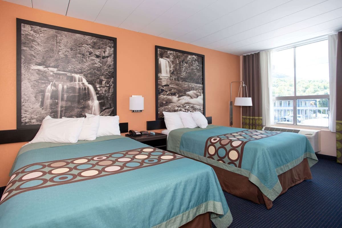 Ett hotellrum med två sängar, stora tavlor i ramar på väggen, ett nattduksbord, en lampa och ett fönster med gardiner.