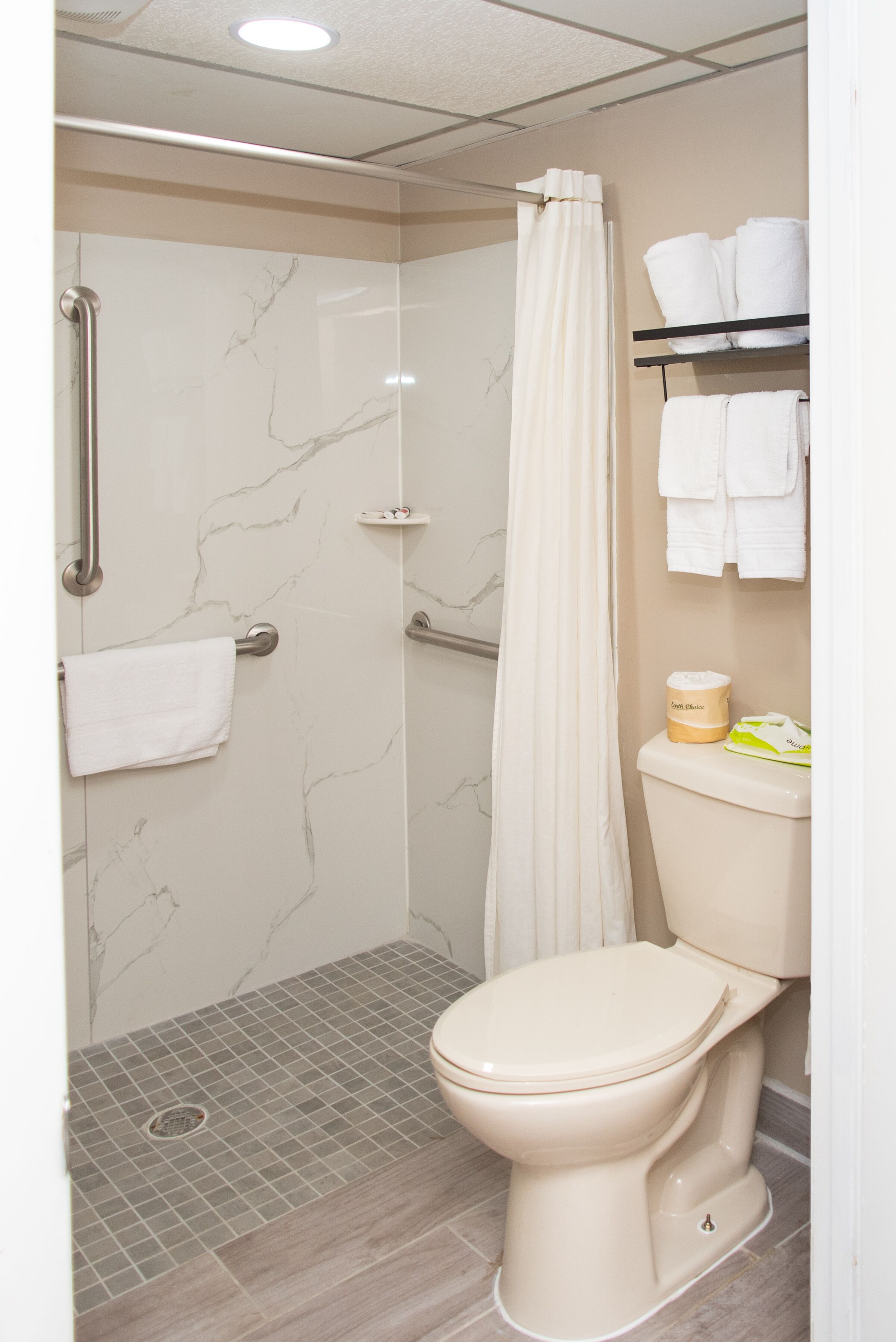 A bathroom with a shower, toilet, and a towel rack with towels.