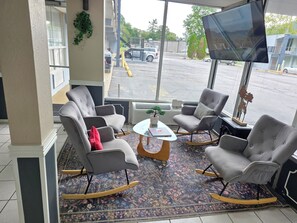 A hotel lobby with a seating area featuring grey upholstered chairs with wooden rockers, a small round coffee table, and a large flat-screen TV mounted on the wall. - Super 8 by Wyndham Black Mountain/Asheville East (Black Mountain)