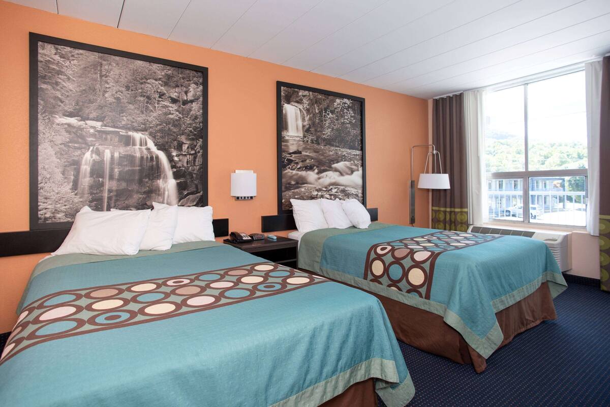 A hotel room with two beds, a large window with a view, and two framed pictures on the wall.