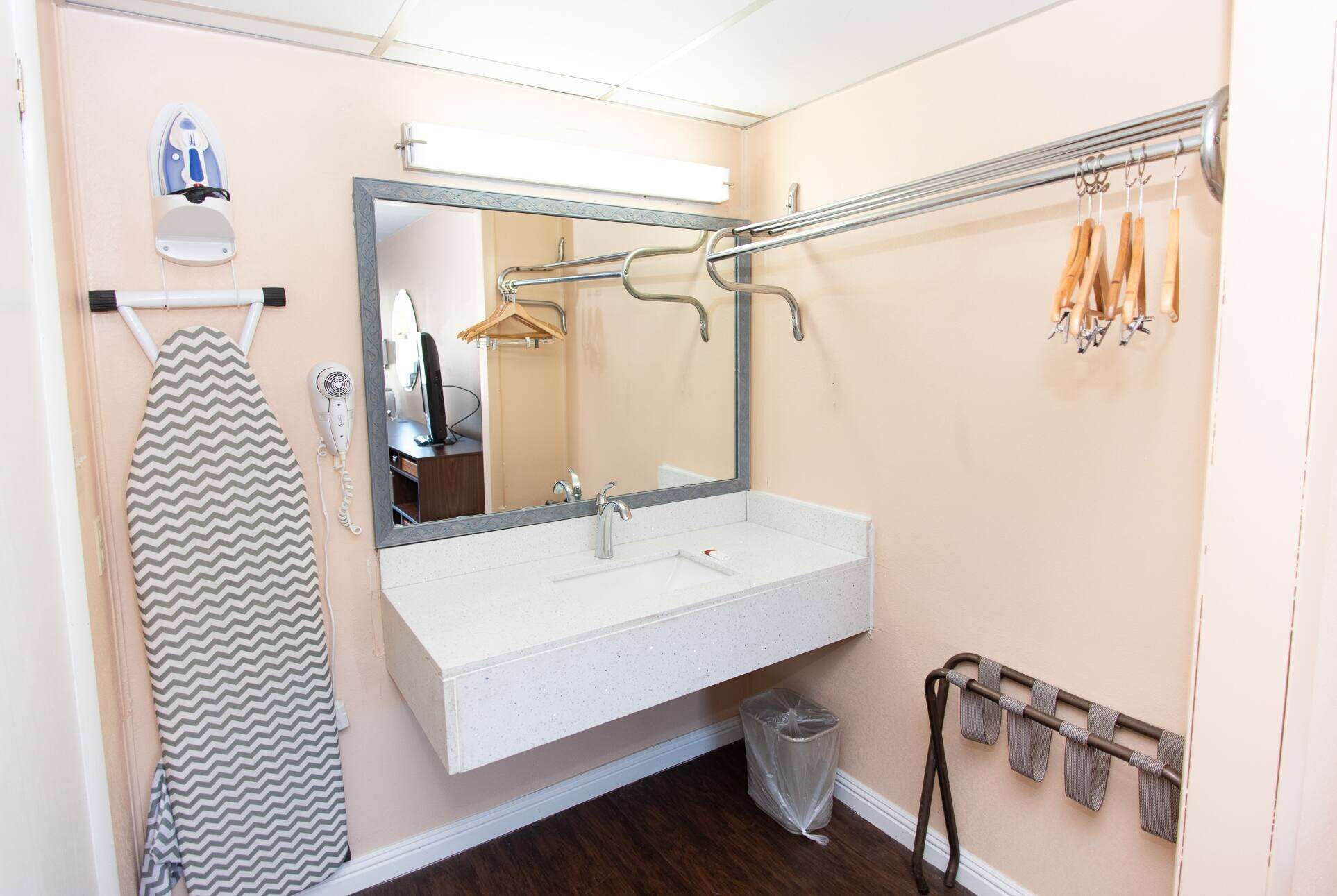 A bathroom with a white sink, a mirror, a towel rack, and a hanging clothes rack.