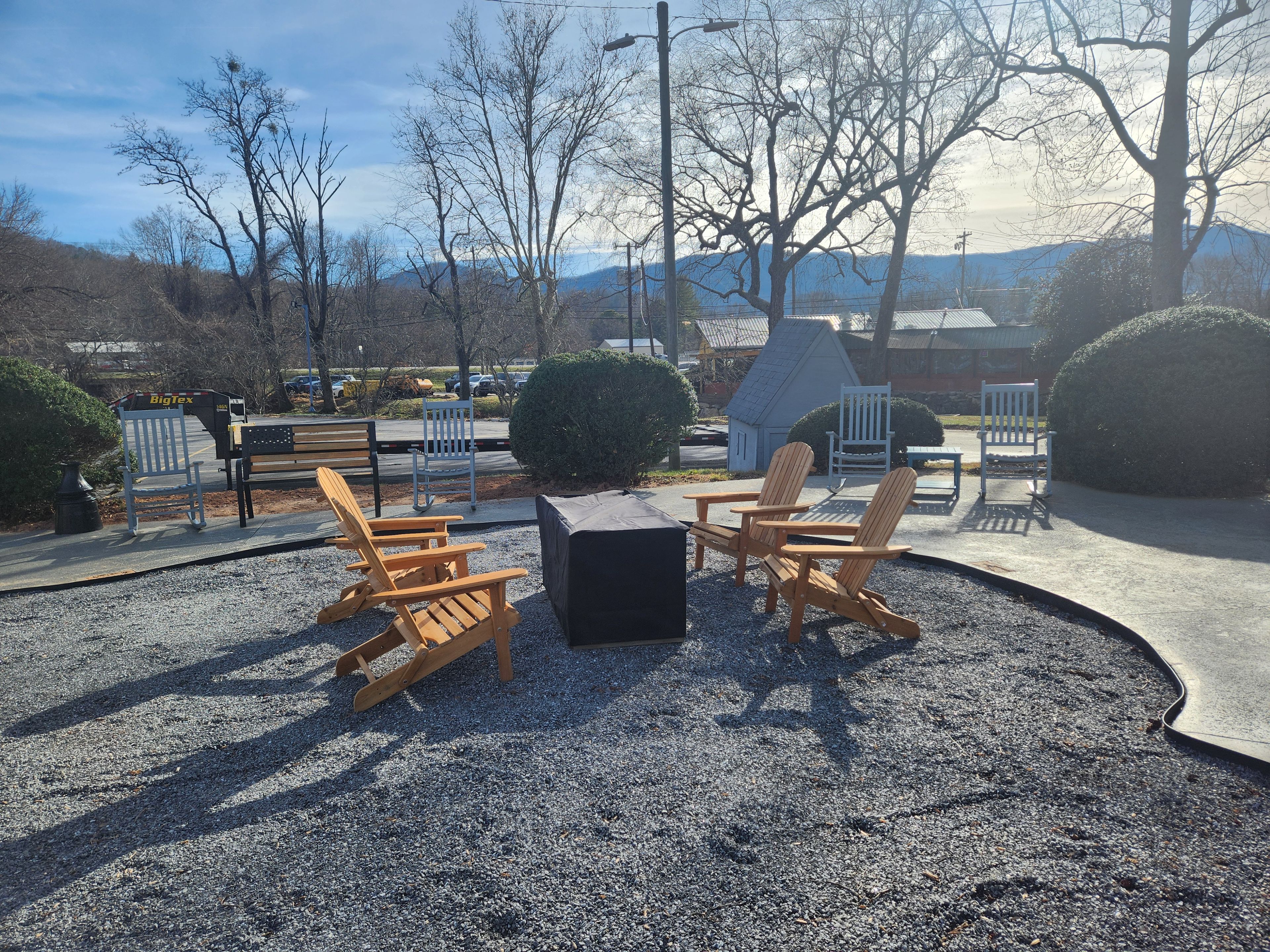 Ein Sitzbereich im Freien mit Adirondack-Stühlen und einem Tisch, umgeben von Kies und Bäumen.
